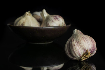 Group of four whole organic white garlic allium sativum in dark ceramic bowl isolated on black glass