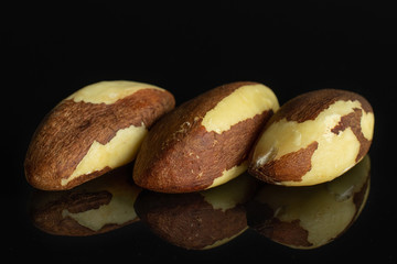 Group of three whole raw brown brazil nut isolated on black glass