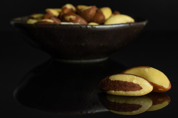 Lot of whole raw brown brazil nut in dark ceramic bowl isolated on black glass