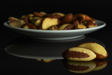 Lot of whole raw brown brazil nut on white ceramic plate isolated on black glass