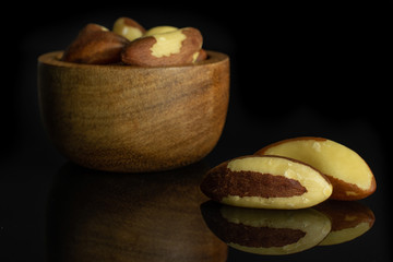 Lot of whole raw brown brazil nut in tiny wooden bowl isolated on black glass