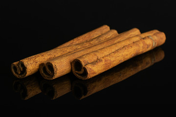 Group of three whole dry brown cinnamon isolated on black glass