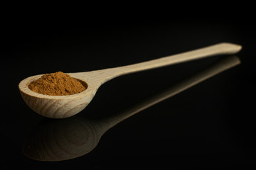 Dry brown cinnamon in a wooden spoon isolated on black glass
