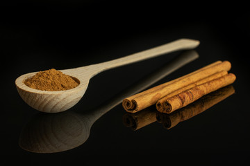 Group of two whole dry brown cinnamon in a wooden spoon isolated on black glass