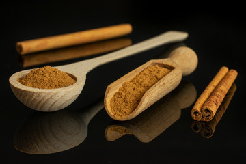 Group of two whole dry brown cinnamon in a wooden spoon in a wooden scoop isolated on black glass