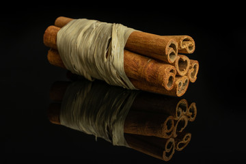Fototapeta na wymiar Group of six whole dry brown cinnamon wrapped in natural bast isolated on black glass