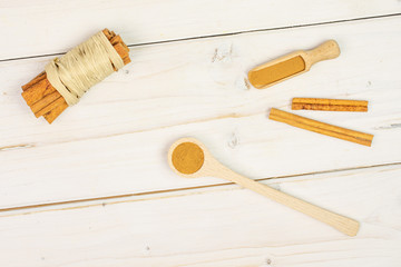 Lot of whole dry brown cinnamon wrapped in natural bast in a wooden spoon in a wooden scoop flatlay...