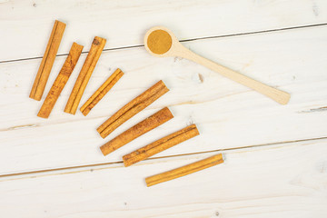 Lot of whole dry brown cinnamon in a wooden spoon flatlay on white wood