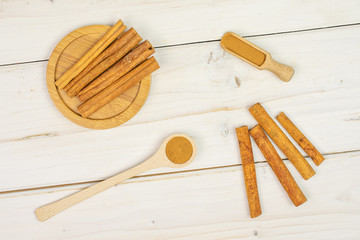 Lot of whole dry brown cinnamon on round bamboo coaster in a wooden spoon in a wooden scoop flatlay on white wood