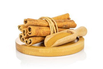 Group of six whole dry brown cinnamon wrapped in natural twine in a wooden scoop on round bamboo coaster isolated on white background