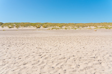 Footsteps in the sand on a beach. Small, grassy hills in the horizon.