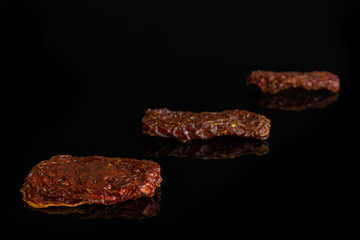 Group of three whole dried red tomato isolated on black glass