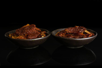 Lot of whole dried red tomato in dark ceramic bowl isolated on black glass