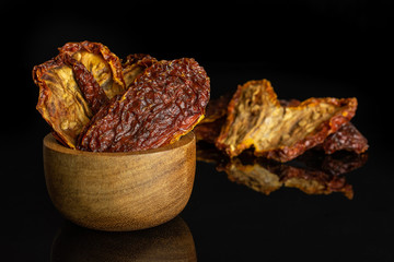 Lot of whole dried red tomato in tiny wooden bowl isolated on black glass