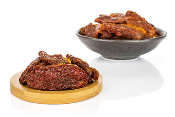 Lot of whole dried red tomato in dark ceramic bowl on round bamboo coaster isolated on white background