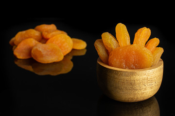 Lot of whole dried orange apricot in tiny wooden bowl isolated on black glass