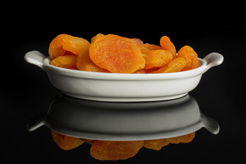 Lot of whole dried orange apricot in white oval ceramic bowl isolated on black glass