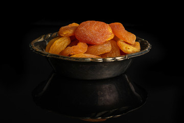 Lot of whole dried orange apricot in metal bowl isolated on black glass