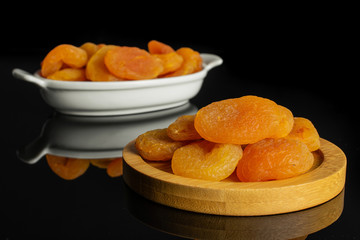 Lot of whole dried orange apricot on round bamboo coaster in white oval ceramic bowl isolated on black glass