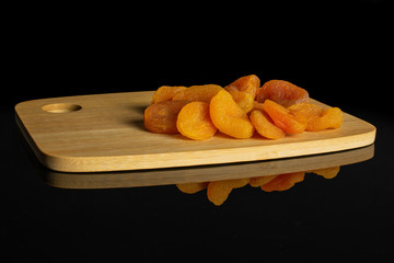 Lot of whole dried orange apricot on bamboo cutting board isolated on black glass