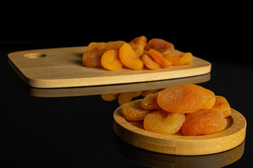 Lot of whole dried orange apricot on round bamboo coaster on bamboo cutting board isolated on black glass