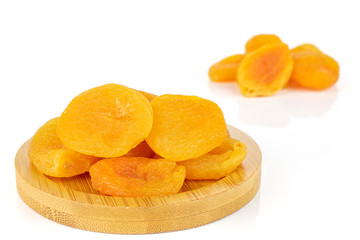 Lot of whole dried orange apricot on round bamboo coaster isolated on white background
