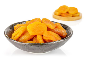 Lot of whole dried orange apricot on round bamboo coaster in dark ceramic bowl isolated on white background