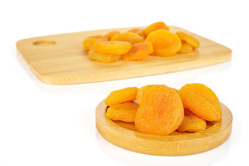 Lot of whole dried orange apricot on round bamboo coaster on bamboo cutting board isolated on white background