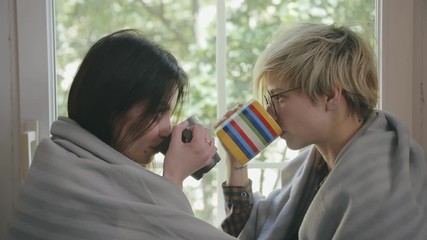 Young homosexual couple drinking coffee at windowsill