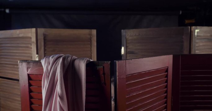 Woman changes clothes behind wooden folding screen.