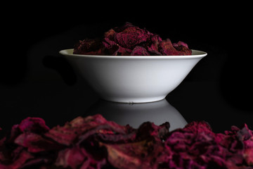 Lot of slices of dried red beetroot in white ceramic bowl isolated on black glass