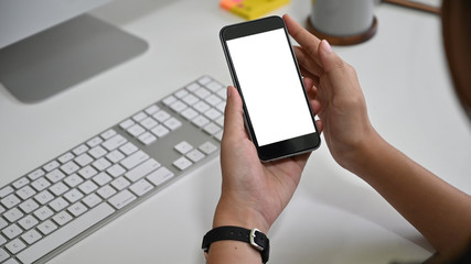 Female's hands holding mockup smartphone empty screen on office desk.