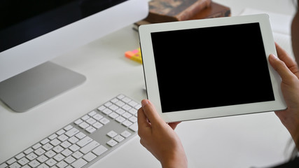 Close-up woman's hands holding mockup tablet empty screen on office desk.