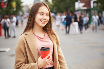 young woman with drink in a paper cup in a city street. Girl with coffee to go.