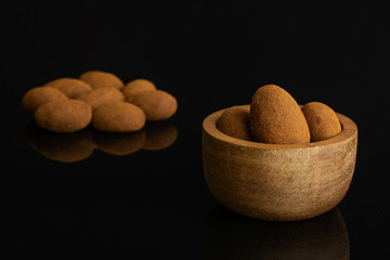 Lot of whole sweet brown chocolate cinnamon almond in tiny wooden bowl isolated on black glass