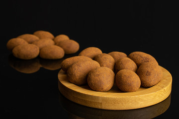 Lot of whole sweet brown chocolate cinnamon almond on round bamboo coaster isolated on black glass