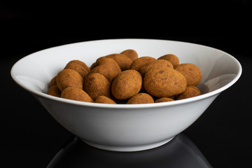 Lot of whole sweet brown chocolate cinnamon almond in white ceramic bowl isolated on black glass