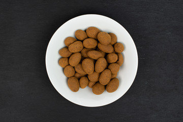 Lot of whole sweet brown chocolate cinnamon almond in white ceramic bowl flatlay on grey stone