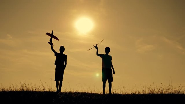 Two boys play with a wooden plane at sunset. Silhouette of children playing with an airplane. Dreams of flying. Children concept. Teamwork. Games and teamwork