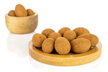 Lot of whole sweet brown chocolate cinnamon almond in tiny wooden bowl on round bamboo coaster isolated on white background