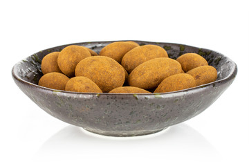 Lot of whole sweet brown chocolate cinnamon almond in dark ceramic bowl isolated on white background