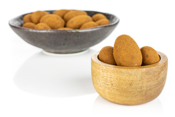 Lot of whole sweet brown chocolate cinnamon almond in tiny wooden bowl in dark ceramic bowl isolated on white background