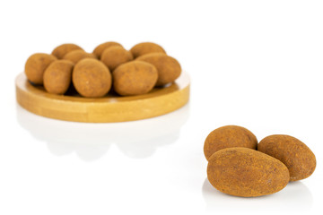 Lot of whole sweet brown chocolate cinnamon almond on round bamboo coaster isolated on white background