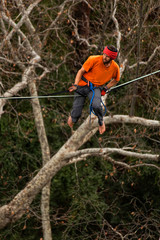 Naklejka premium A man is walking along a stretched sling. Highline in the mountains. Man catches balance. Performance of a tightrope walker in nature. Highliner on the background of valley.