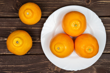 Group of five whole fresh orange tangelo minneola on white ceramic plate flatlay on brown wood