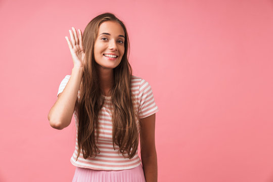 Cheery young pleased girl posing isolated over pink wall background try to hear you.