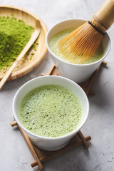 Matcha green tea in two white Tawan, tasaku and a bamboo whisk on white concrete background