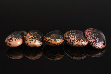 Group of five whole stained purple bean isolated on black glass