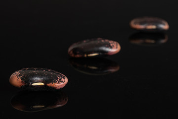 Group of three whole stained purple bean placed diagonally isolated on black glass