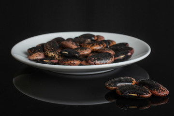 Lot of whole stained purple bean on white ceramic plate isolated on black glass